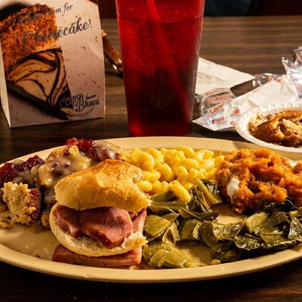 A full plate of Southern comfort food, including ham biscuits, mac and cheese, collard greens, and sweet potatoes.