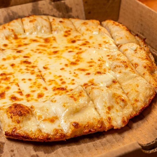 Cheesy breadsticks with melted mozzarella and a side of marinara sauce in a cardboard box.
